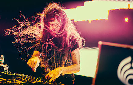 EDM artist and DJ Bassnectar with long hair blowing in wind working on DJ set. 