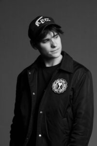 DJ Audien wearing black, black and white photo, black hat and jacket.